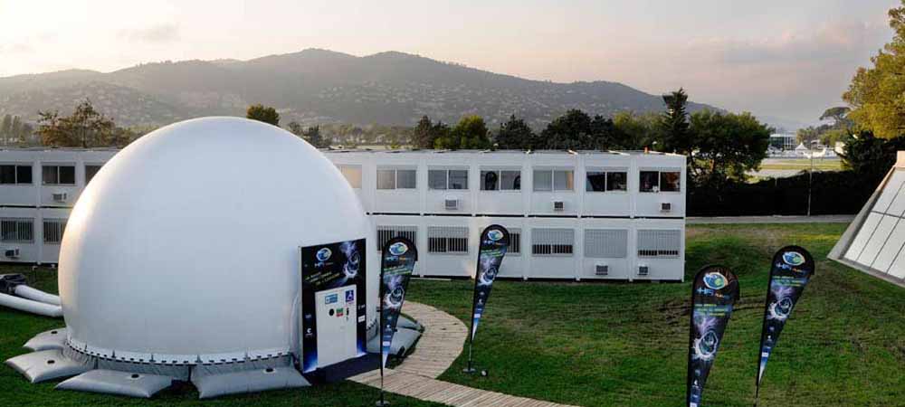 Dôme gonflable installé en extérieur pour une animation ou une exposition, avec des bannières publicitaires et un paysage montagneux en arrière-plan